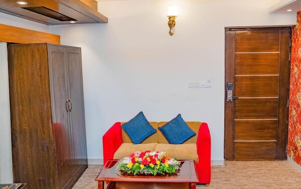 A room with a sofa, a coffee table with flowers, a wardrobe, and a door. - Air Inn (Dhaka)