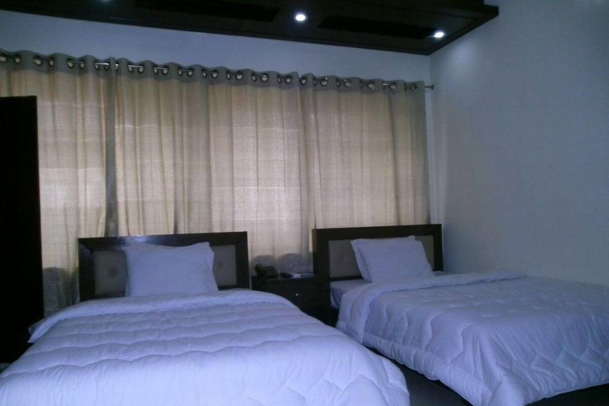 A room with two beds, a nightstand, and a window with curtains.