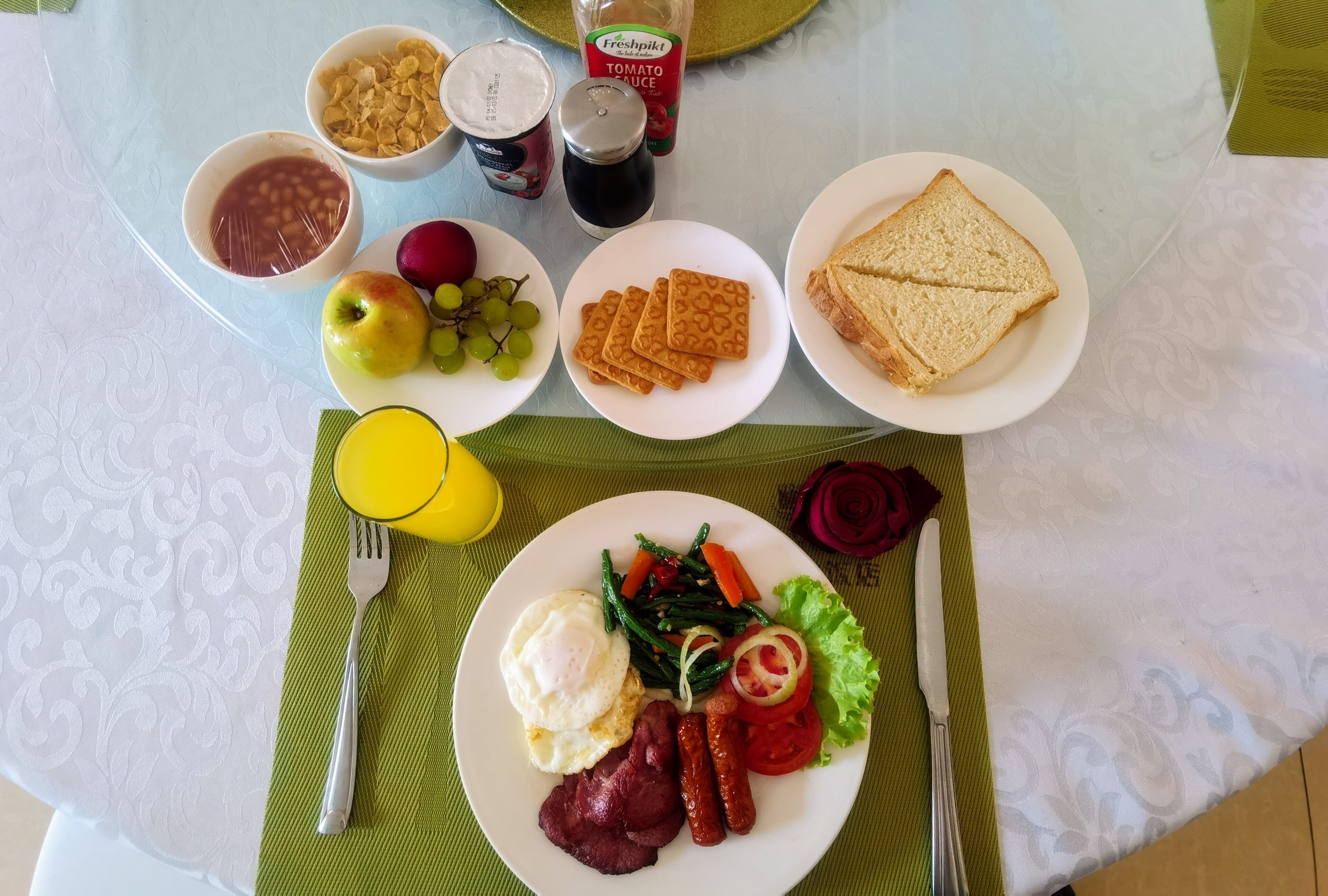 Aamiaispöytä, jossa on monenlaista tarjottavaa, kuten paahtoleipää, kananmunia, makkaroita ja vihanneksia.
