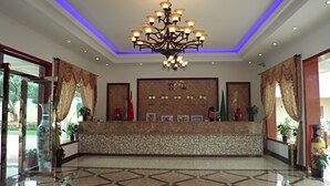 A reception area with a chandelier, a wall with framed photos, and a tiled floor. - Oriental Swan Hotel Livingstone (Livingstone)