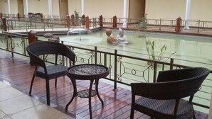 A covered outdoor seating area with wicker chairs and a round table, overlooking a water feature with rocks and a statue. - Oriental Swan Hotel Livingstone (Livingstone)