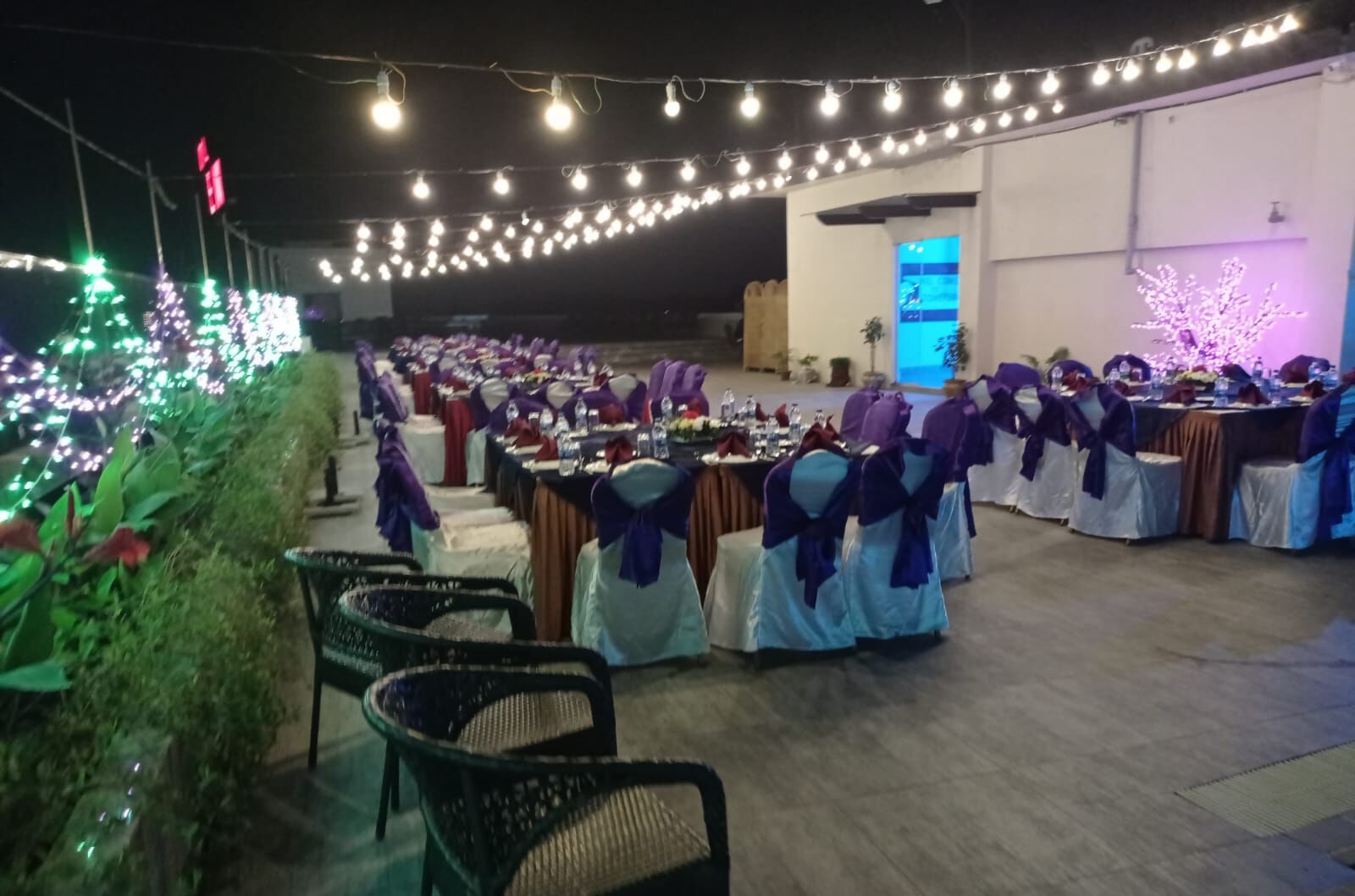 A banquet hall with rows of tables, chairs, and string lights.