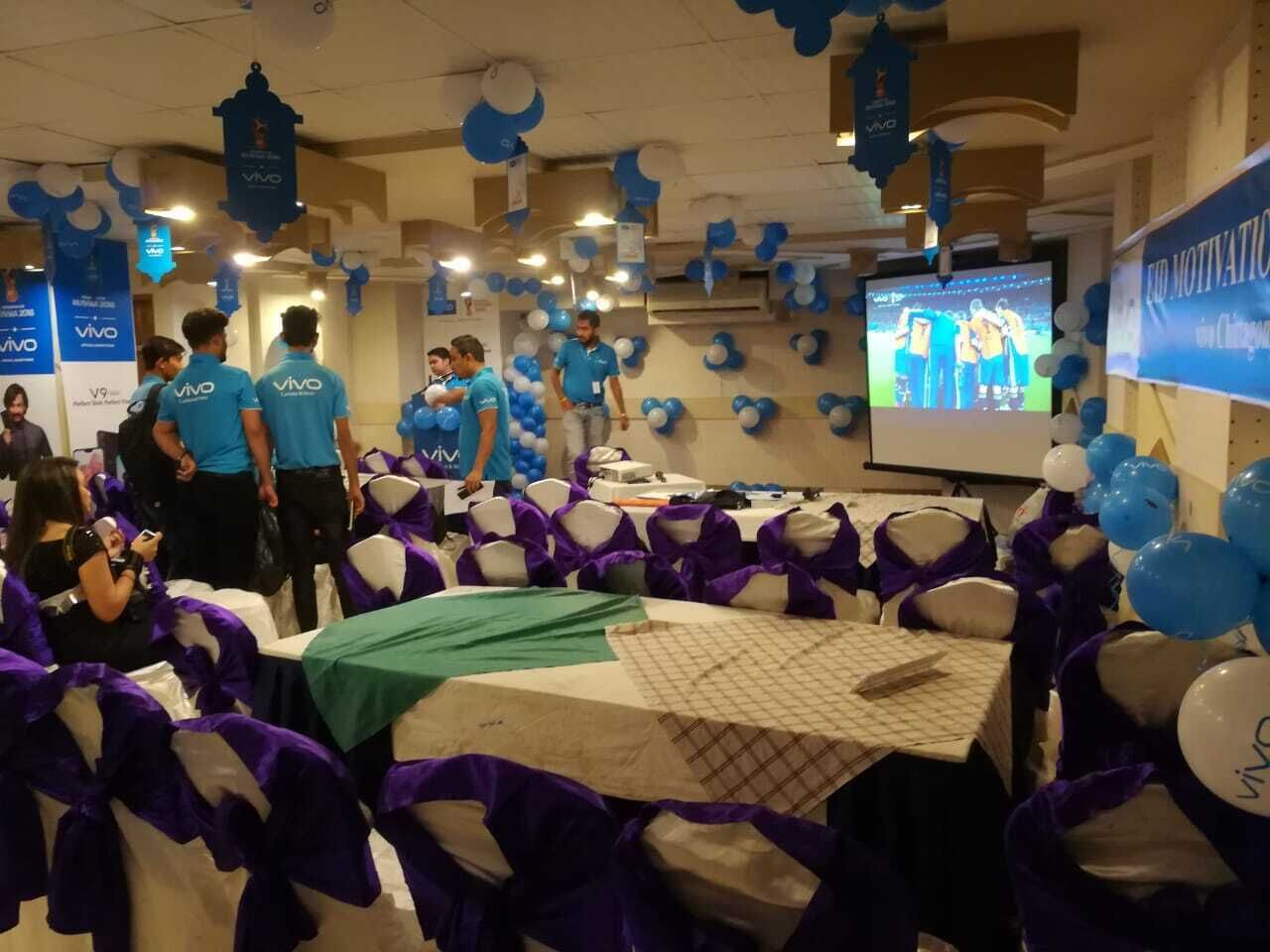 Ett konferensrum med bord täckta av vita dukar, stolar dekorerade med lila band och blåa och vita ballonger.
