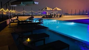 A pool area with lounge chairs and umbrellas, surrounded by string lights. - Hotel Tower Inn (Chittagong)