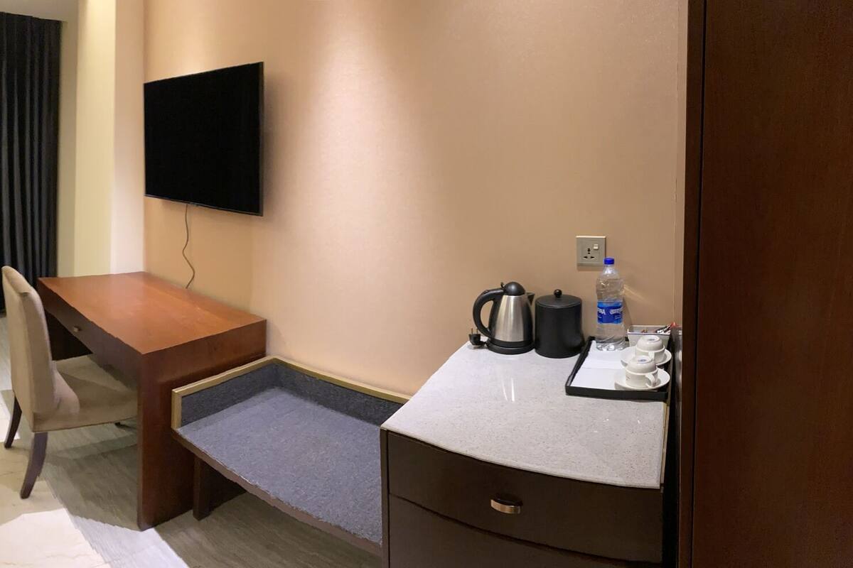 A hotel room with a bed, a desk, a chair, a TV, and a minibar.