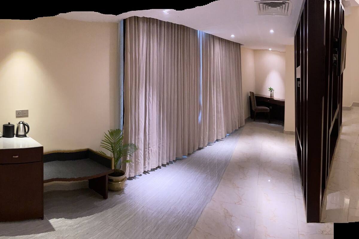 A hotel room with a bed, a desk, a chair, a sofa, and a TV.