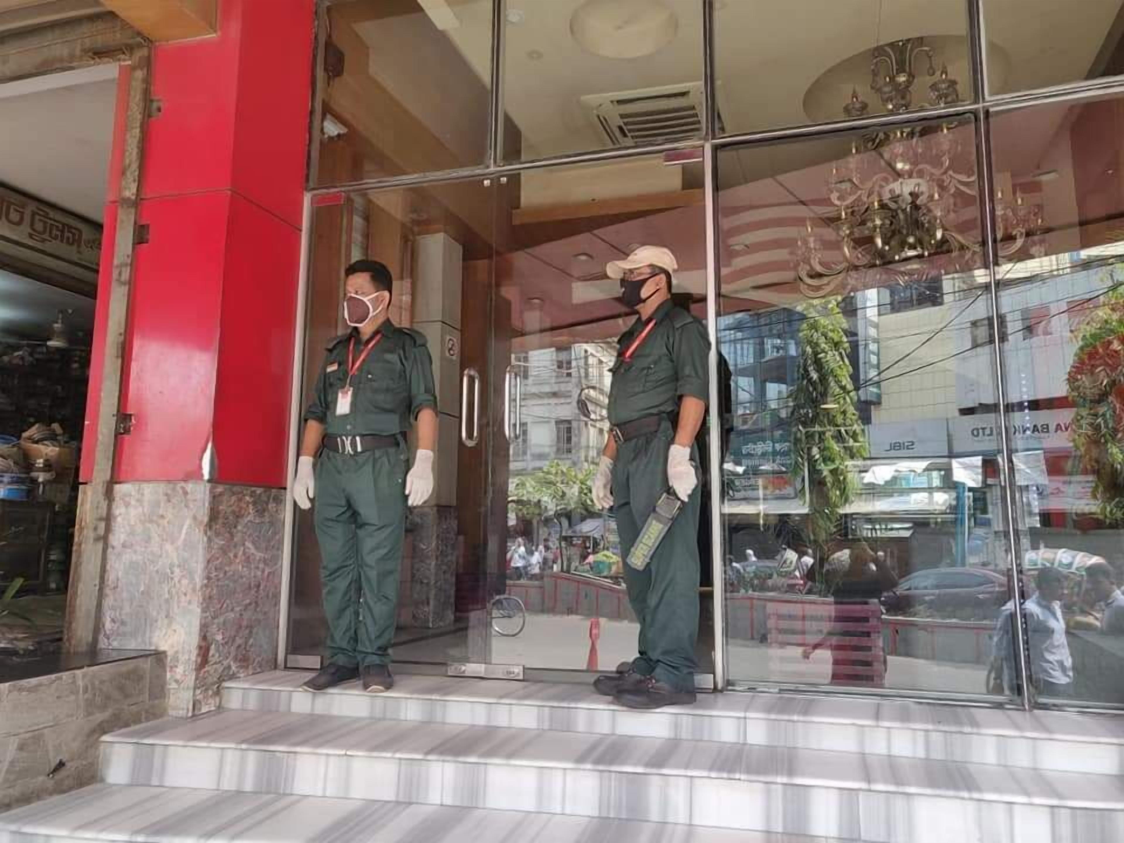 Two uniformed security guards standing at the entrance of a building with a red pillar and glass doors.