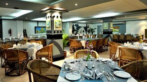 A restaurant with multiple dining tables set with white tablecloths, surrounded by wicker chairs. - Hotel Tower Inn (Chittagong)
