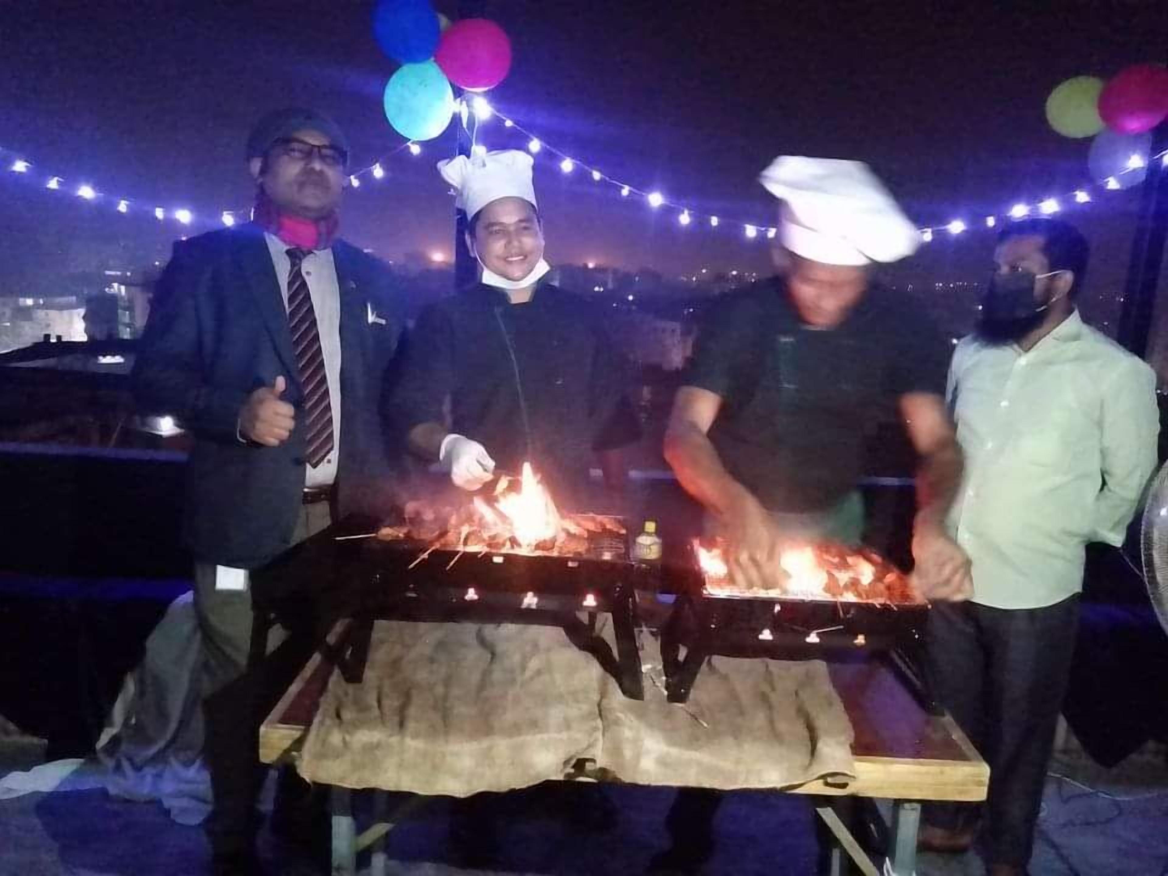 A group of people around a grill with food being cooked outdoors at night.