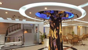 A lobby with a central decorative column, a staircase, and a dining area with wicker chairs. - Hotel Tower Inn (Chittagong)