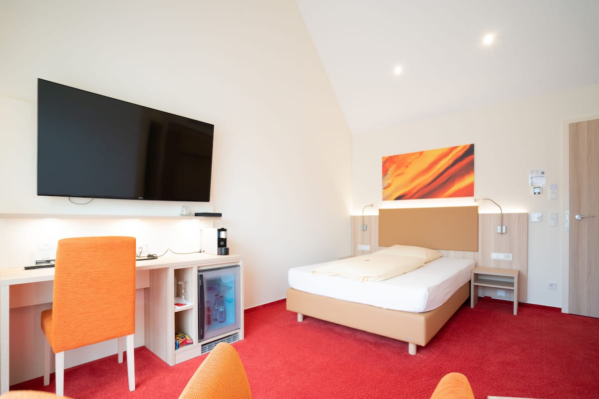 A hotel room with a bed, a desk, a television, and a small refrigerator.