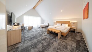 Une chambre d’hôtel moderne avec un plafond en pente, un grand lit, un bureau avec un ordinateur, un canapé et un téléviseur.