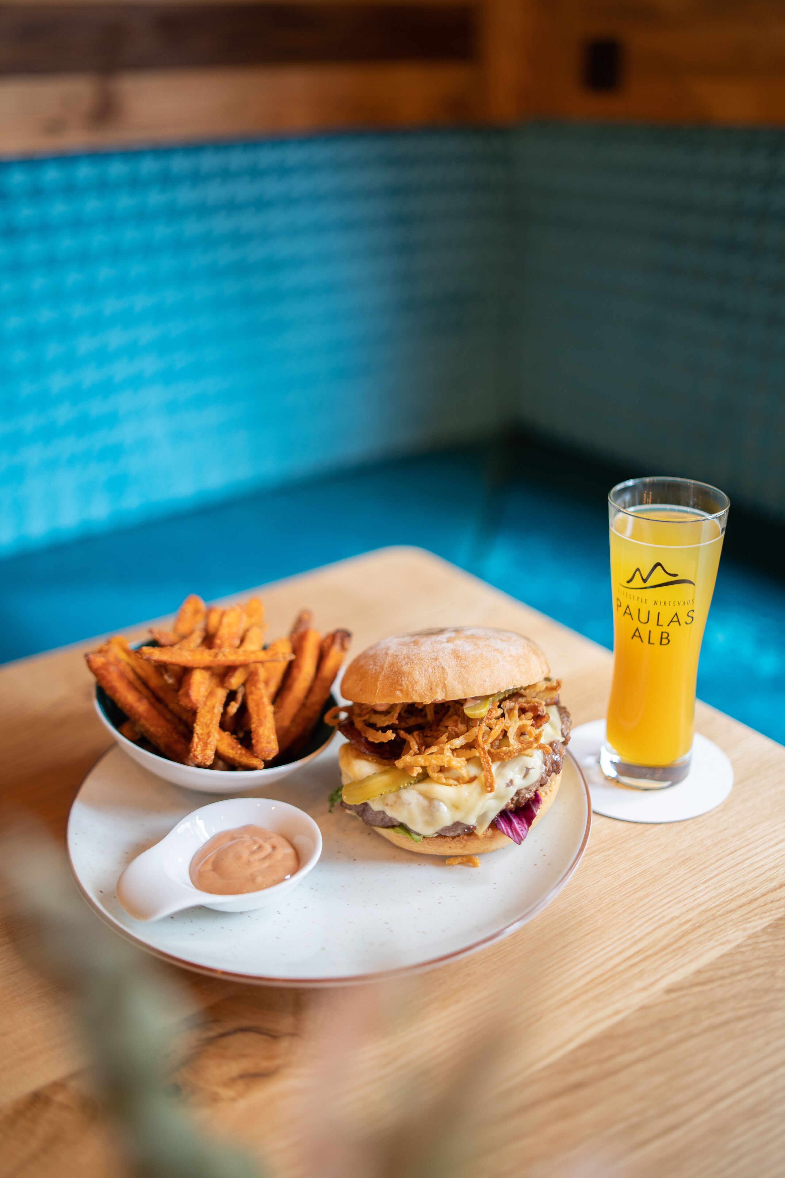 A plate with a burger, fries, and a glass of beer on a wooden table.