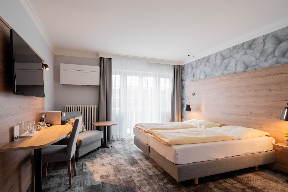 A modern hotel room with a bed, a desk, a chair, a small table, and a TV.