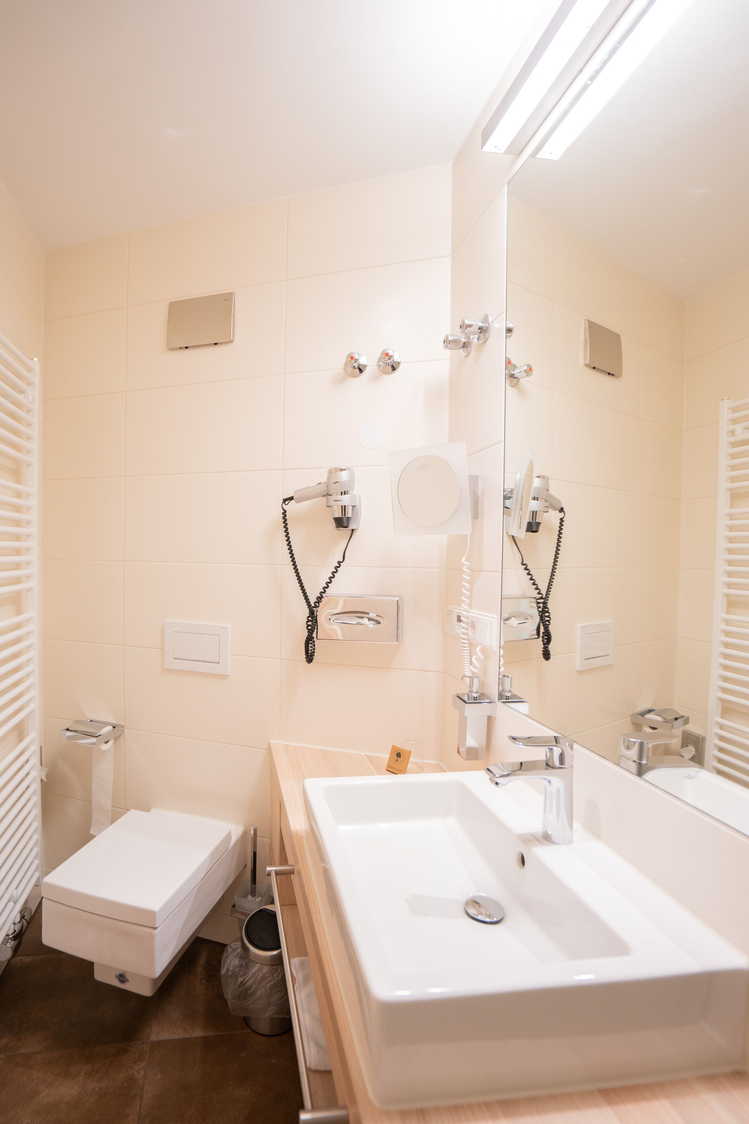 A modern bathroom with a large mirror, two sinks, and a toilet.