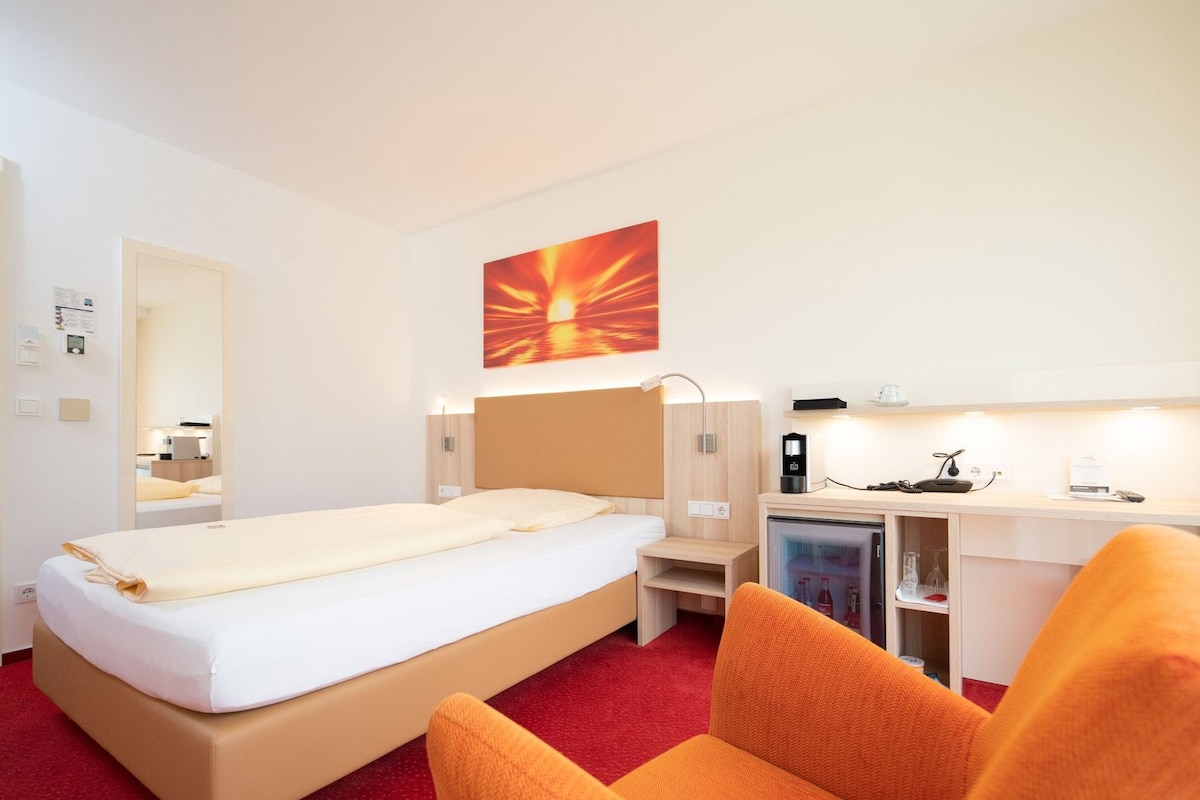 A hotel room with a bed, a desk with a computer, a refrigerator, and a chair.