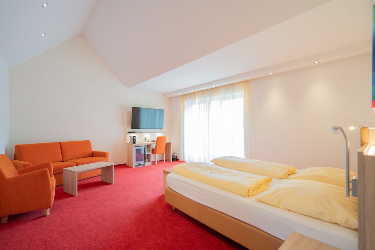 A hotel room with a large bed, a sofa, a desk, and a TV.