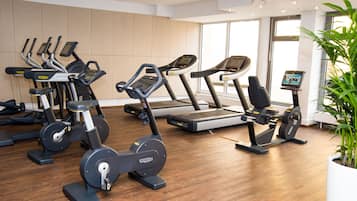 Ein Fitnessstudio mit verschiedenen Trainingsgeräten, einem großen Fenster und einer Zimmerpflanze.