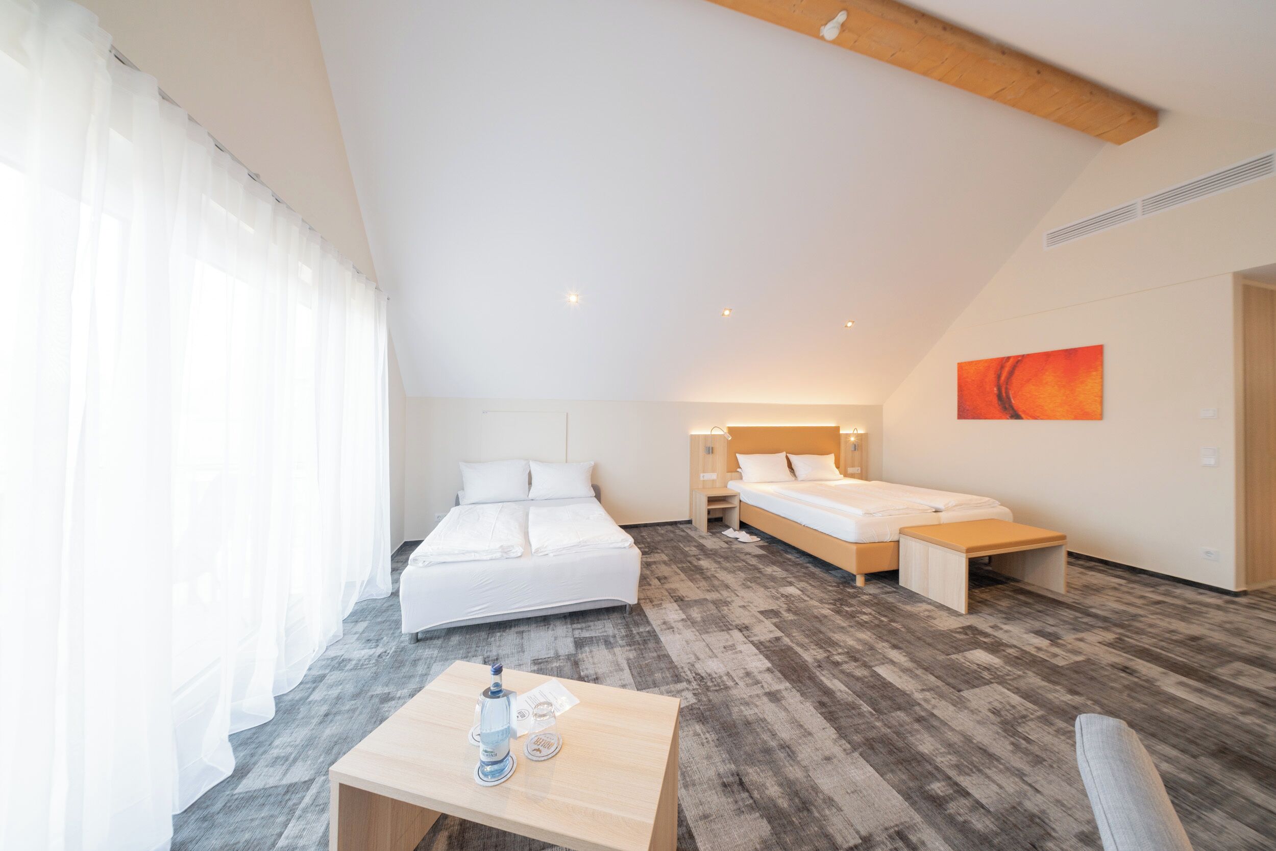 A modern hotel room with a large bed, a smaller bed, a desk with a chair, and a painting on the wall.