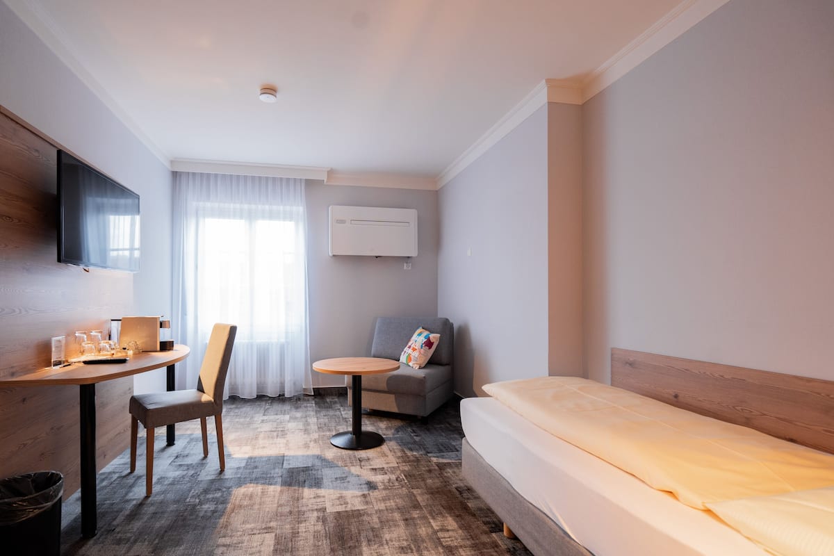 A hotel room with a bed, a desk with a chair, a small table, a sofa, and a TV mounted on the wall.