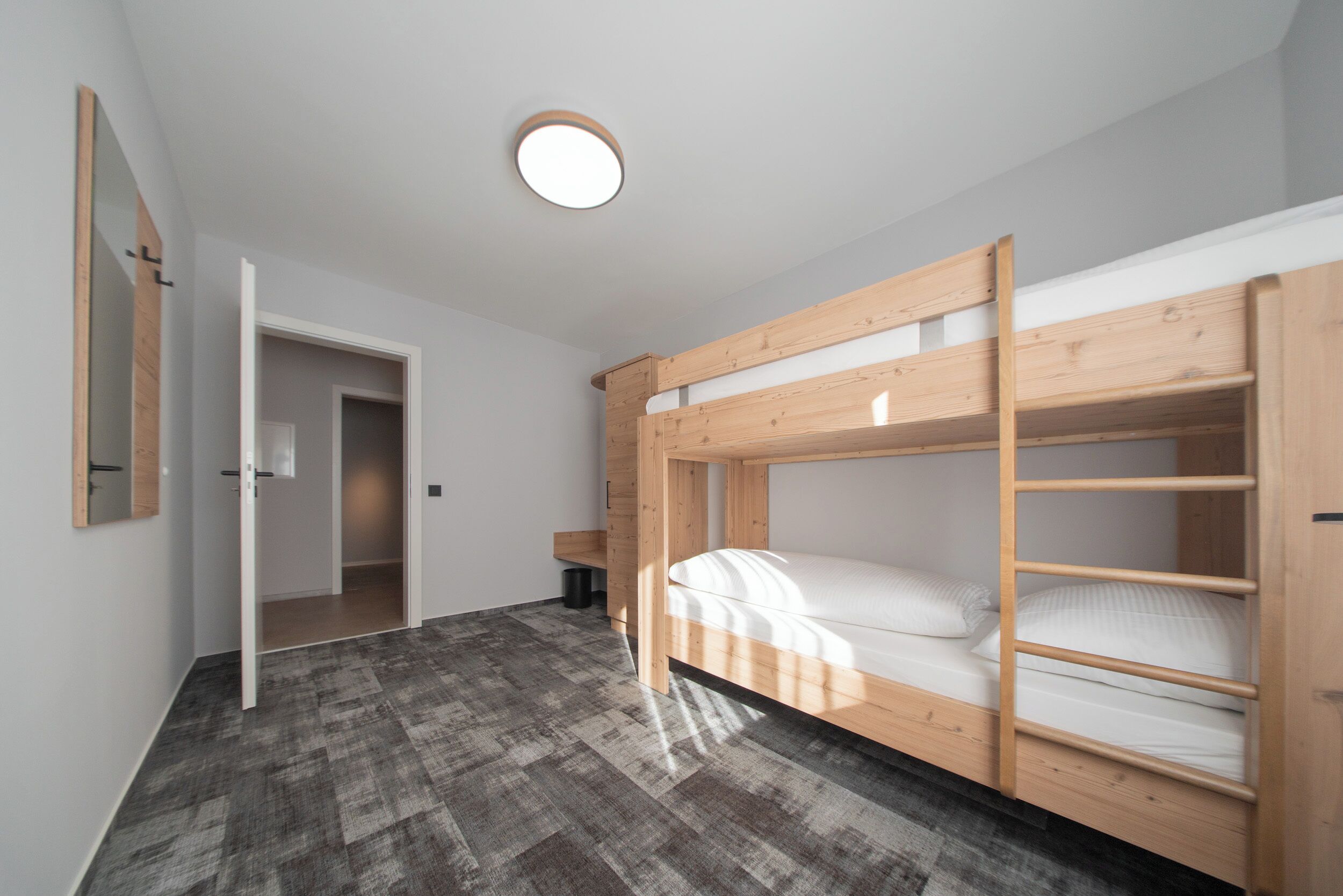 Une pièce avec un lit superposé, un miroir, une porte et un luminaire au plafond.