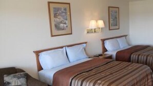 A hotel room with two beds, a nightstand, a lamp, and framed pictures on the wall. - Coho Motel and Suites (Kewaunee)