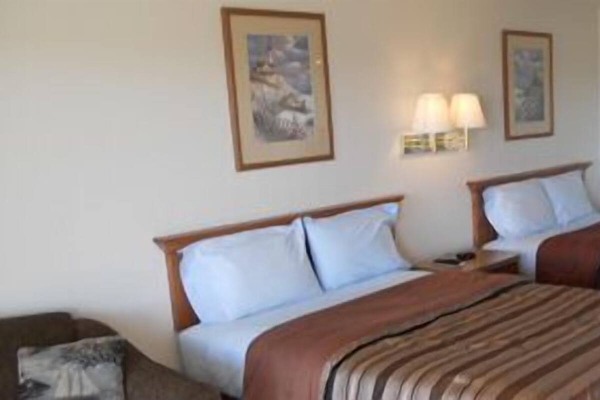 A hotel room with two beds, a nightstand, a lamp, and framed pictures on the wall.