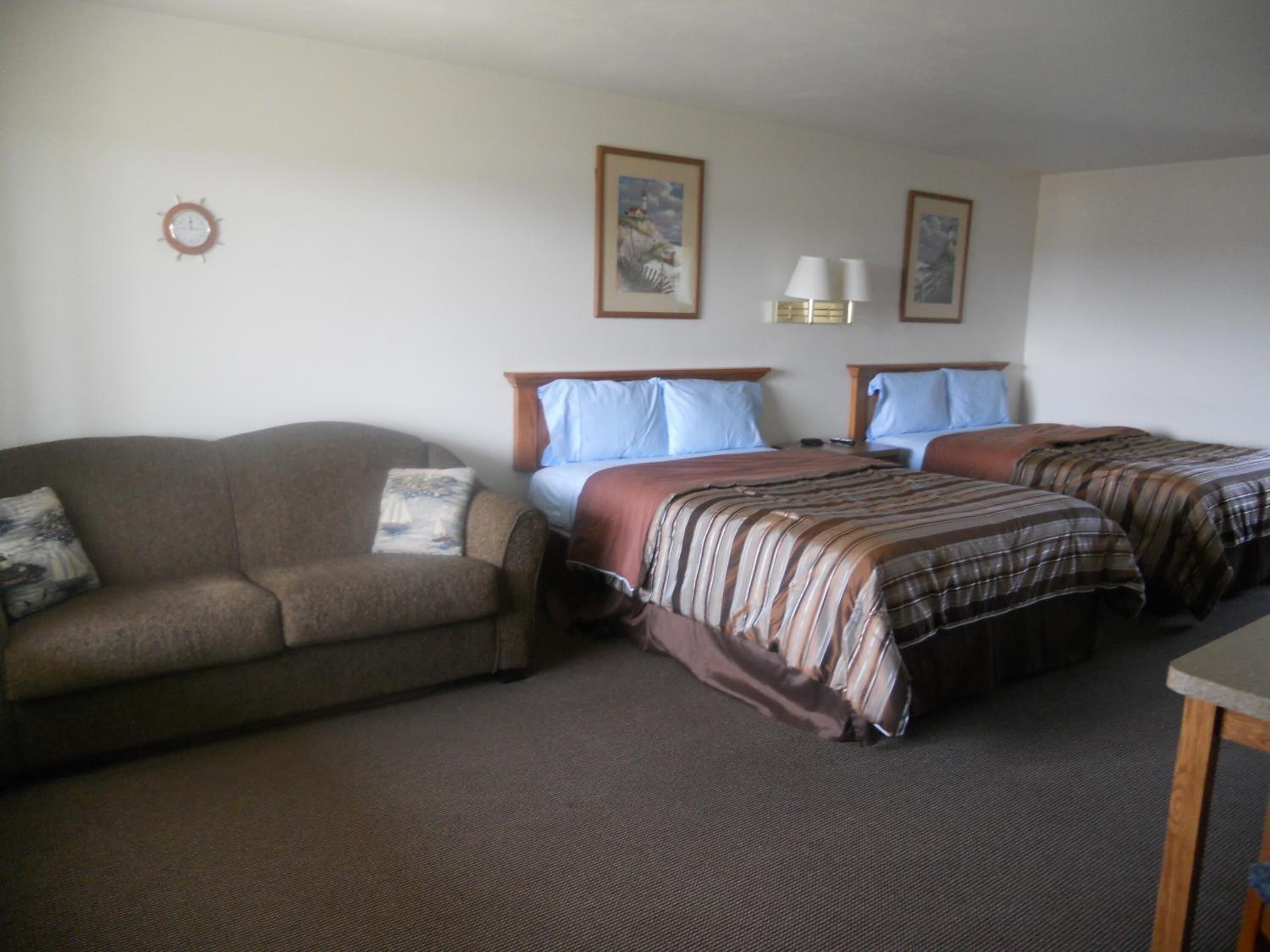 A hotel room with a sofa, two single beds, a nightstand, and a lamp.