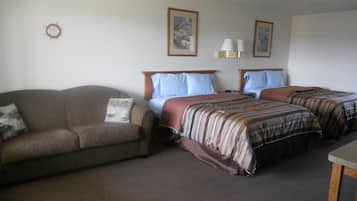 A hotel room with a sofa, two single beds, a nightstand, and a lamp.