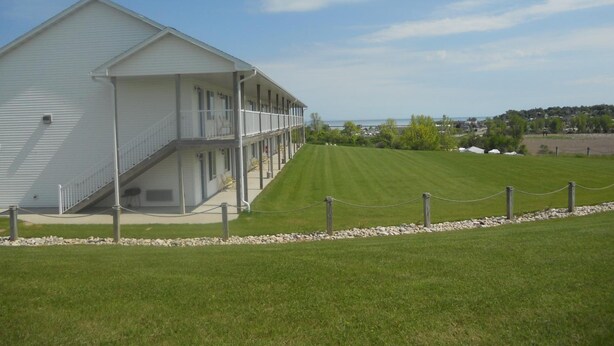 A two-story motel with a covered outdoor seating area and a view of the ocean. - Coho Motel and Suites (Kewaunee)