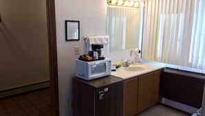 A hotel bathroom with a sink, mirror, and a microwave on a cabinet. - Coho Motel and Suites (Kewaunee)