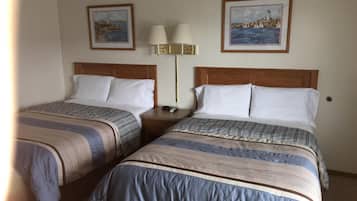 Une chambre d’hôtel avec deux lits, chacun doté d’une literie à rayures, d’une tête de lit en bois et d’une table de chevet avec une lampe. Deux tableaux encadrés sont accrochés au mur, au-dessus des lits.