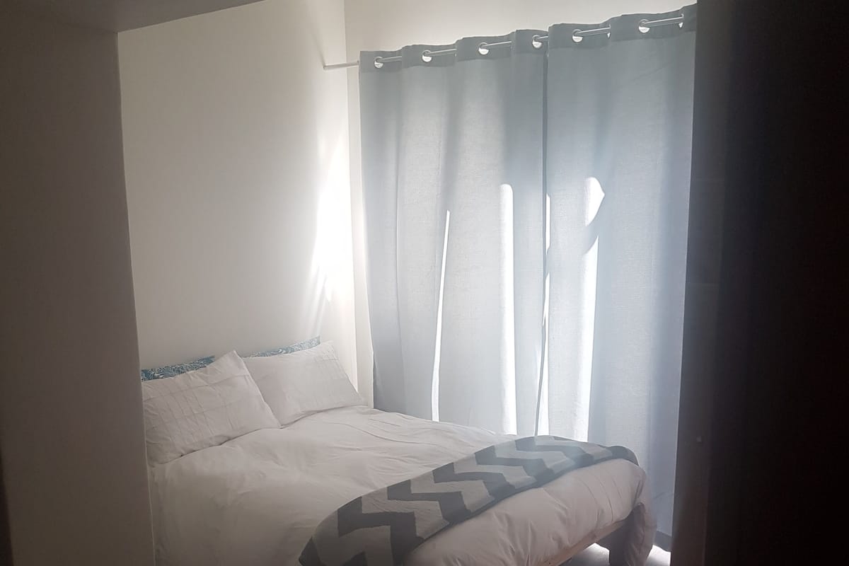 A bedroom with a bed, a window with curtains, and a colorful rug.