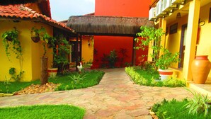 Un patio con un camino de piedra, plantas en macetas y una estructura con tejado de paja.