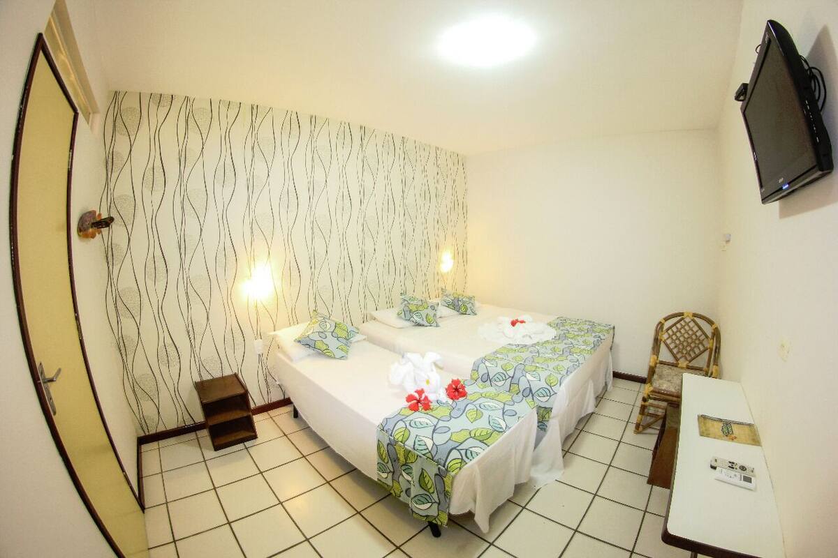 Una habitación pequeña y limpia con dos camas, una silla, una mesa y un televisor.