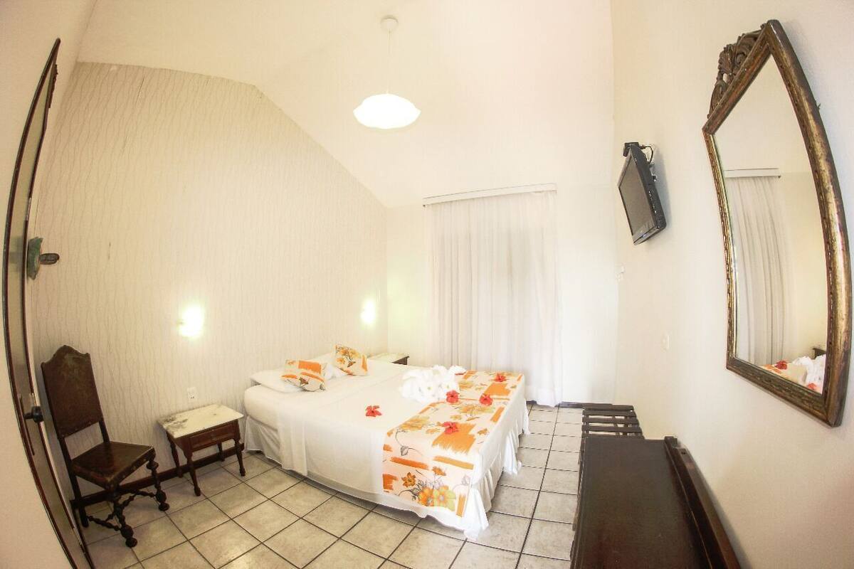 Una habitación de hotel con una cama, una silla, un escritorio, un espejo y una ventana con cortinas.