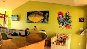 Una zona de recepción con mostrador, televisor, un cuadro de un pez y un gallo en la pared.