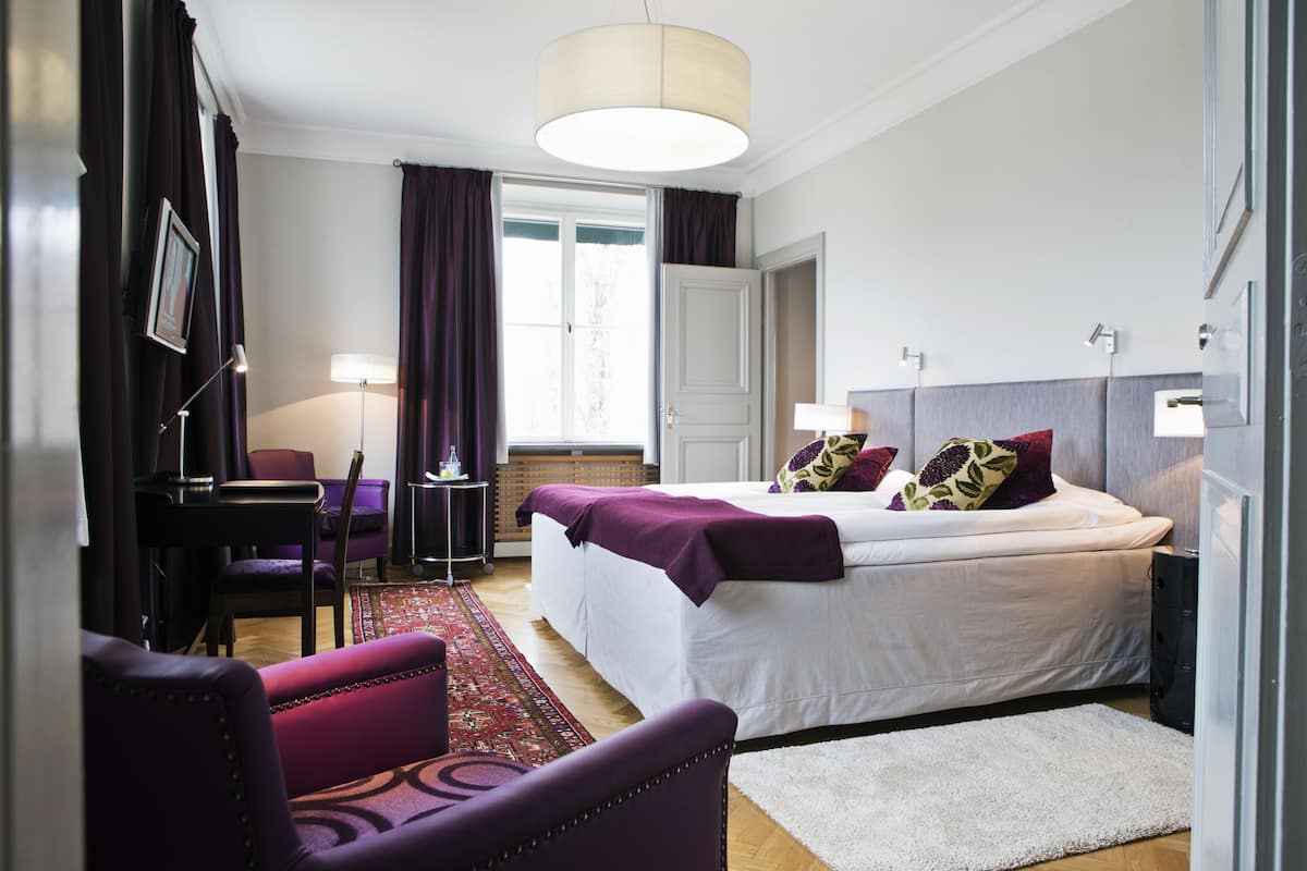 Habitación de hotel con una cama grande, un escritorio con silla, un sofá y un televisor en la pared.