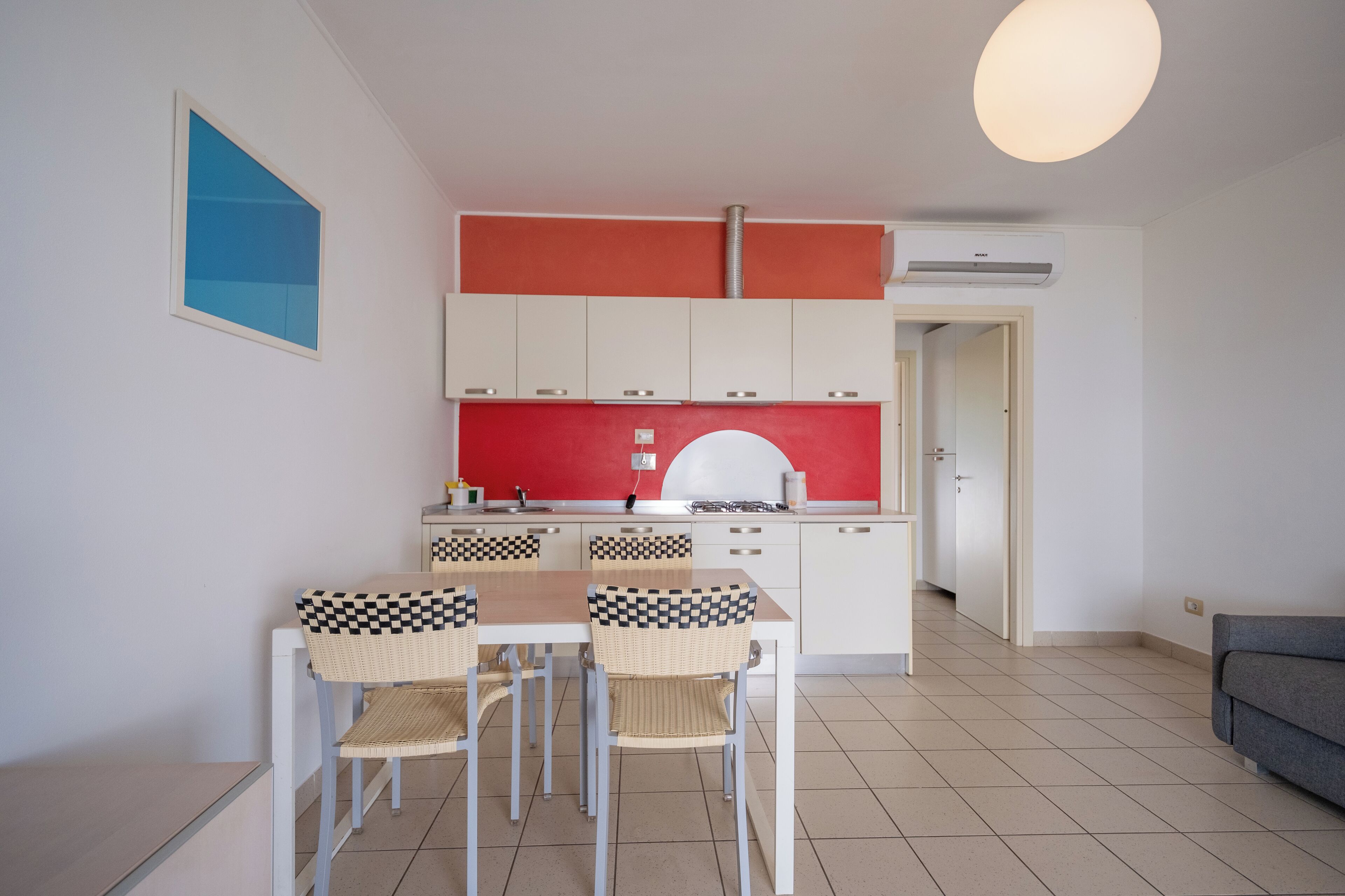 Una cocina compacta con una mesa y sillas, un salpicadero rojo y armarios blancos.