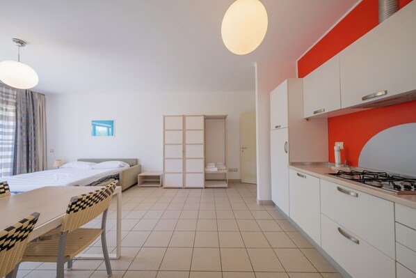 A modern hotel room with a dining area, kitchenette, and a bed with a view. - Residence Solidago (Pisa)