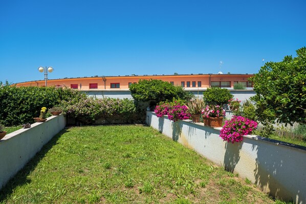 Un cortile con un'area verde, piante in vaso e un edificio con tetto rosso.