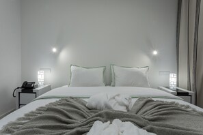 A neatly made bed with white linens and a gray blanket, two bedside lamps, and a phone on a bedside table.