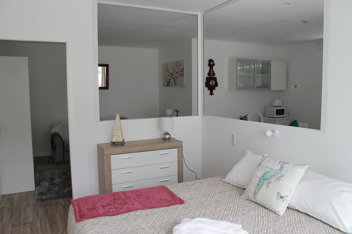 A bedroom with a bed, a dresser, a mirror, a nightstand, and a small desk with a lamp.