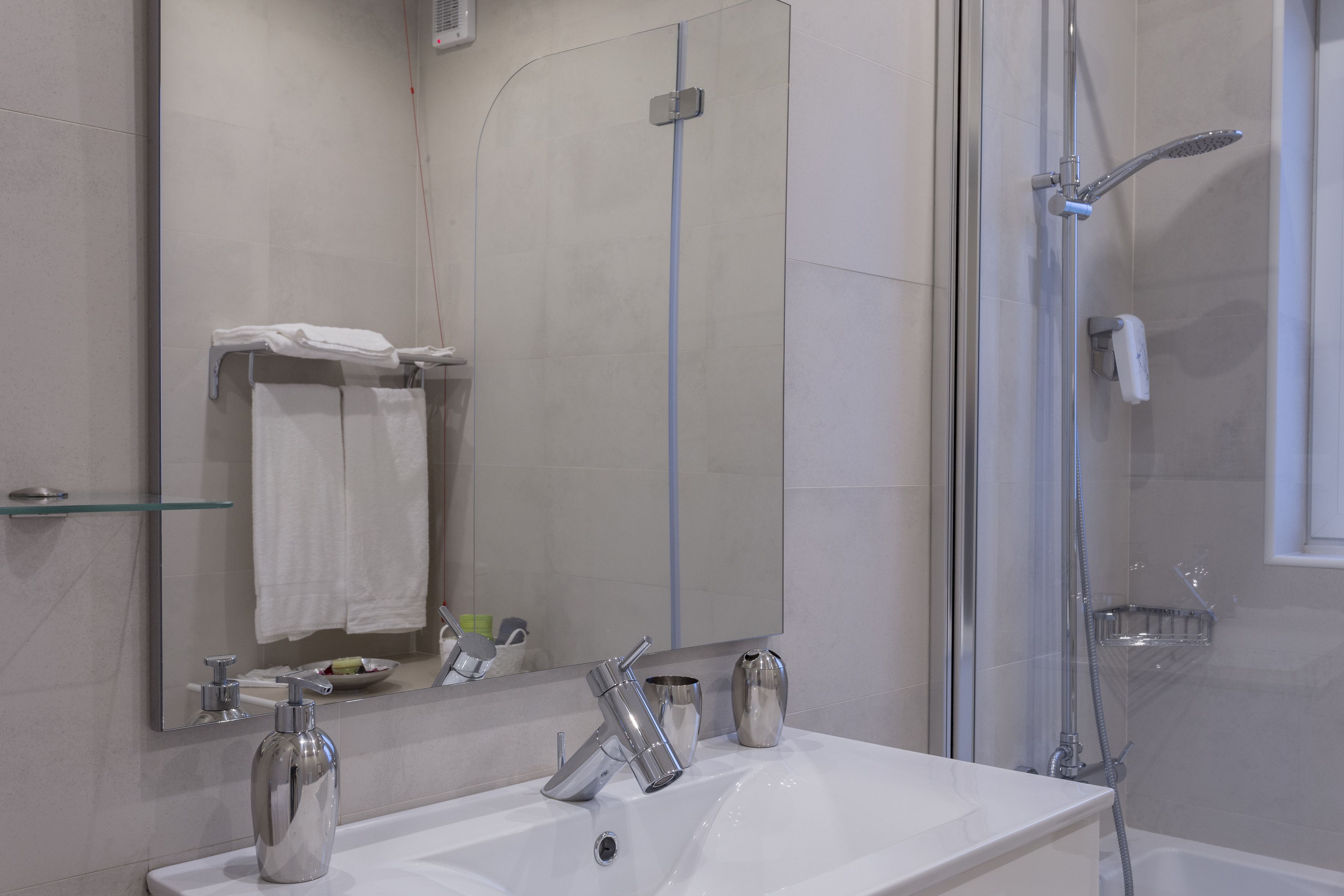 Une salle de bain moderne avec un grand miroir, un lavabo blanc, une douche et une étagère en verre.
