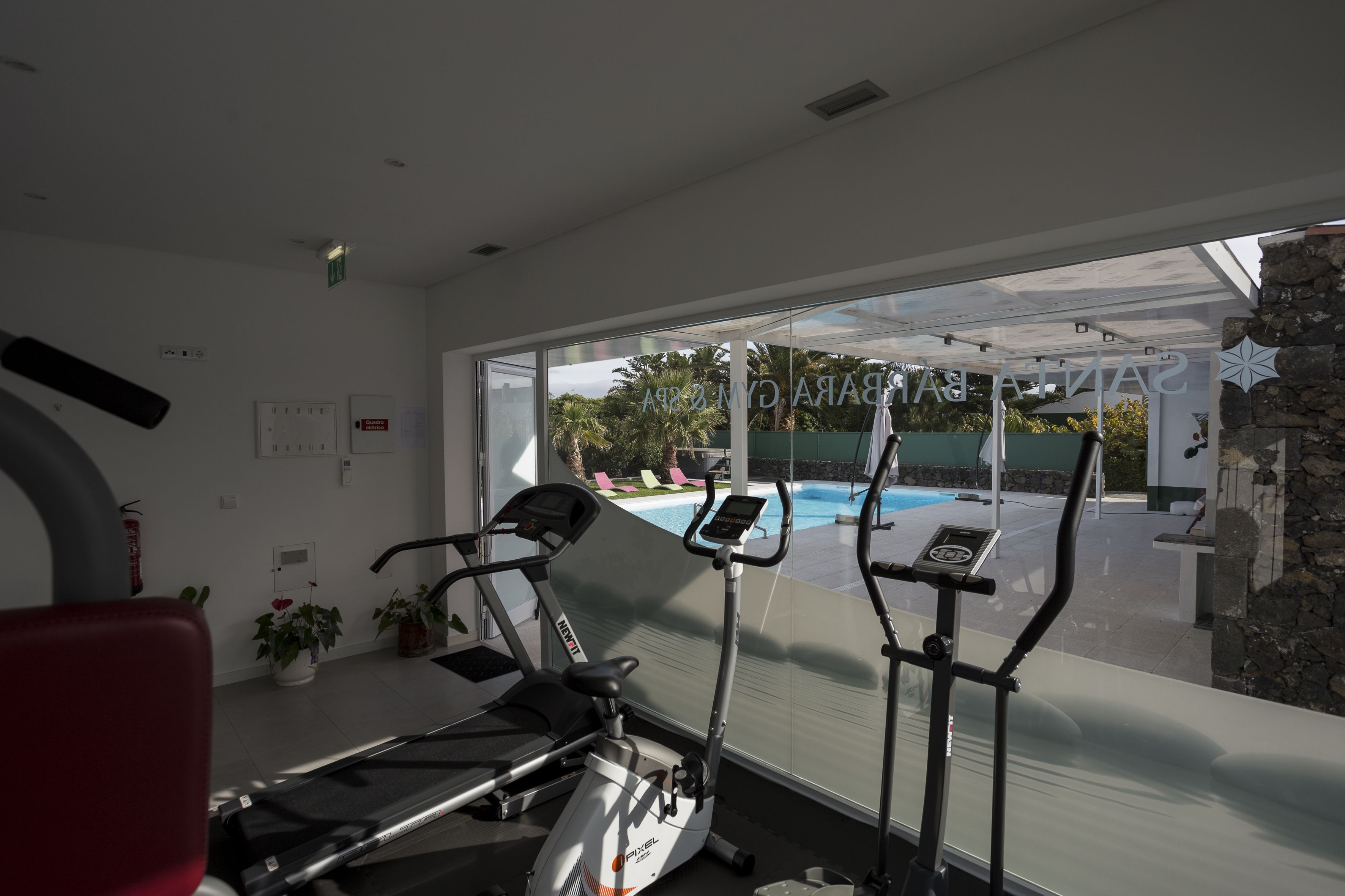 Un gimnasio con equipo de ejercicio, un ventanal con vista a una piscina y zona exterior.