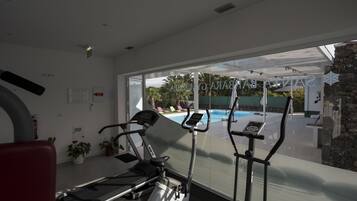 Un gimnasio con equipo de ejercicio, un ventanal con vista a una piscina y zona exterior.