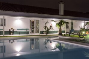 A poolside area with a clear pool, lounge chairs, and a well-lit building with a tiled roof. - Quinta de Santa Bárbara Casas Turisticas (Lagoa)