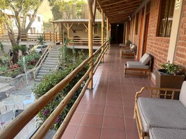 Un espacio al aire libre techado con barandilla de madera, muebles de mimbre y plantas en macetas.