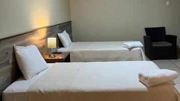 Et hotelværelse med to senge, et natbord, en stol og en loftslampe.