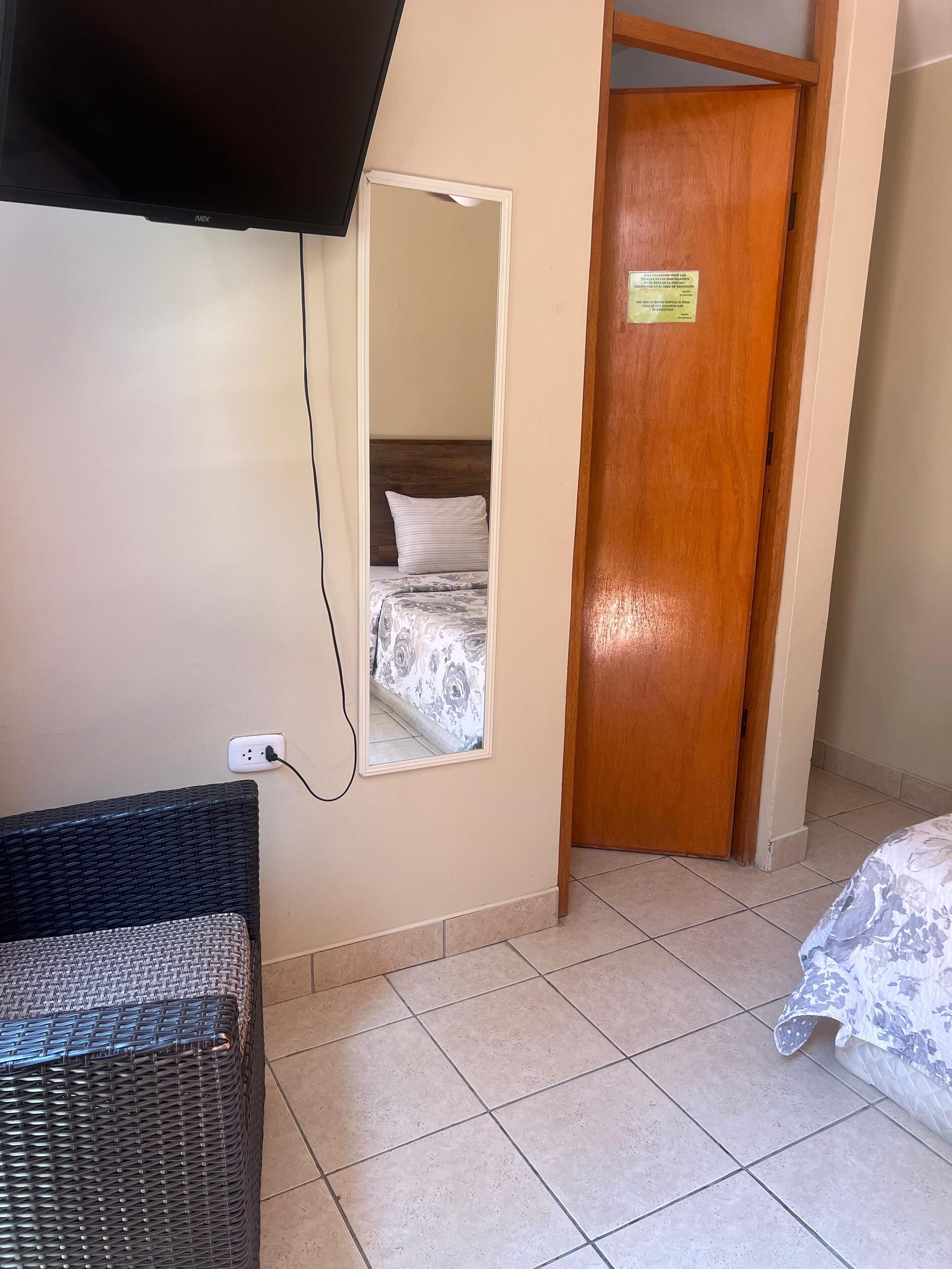 A room with a bed, a television mounted on the wall, a wooden door, and a power outlet.
